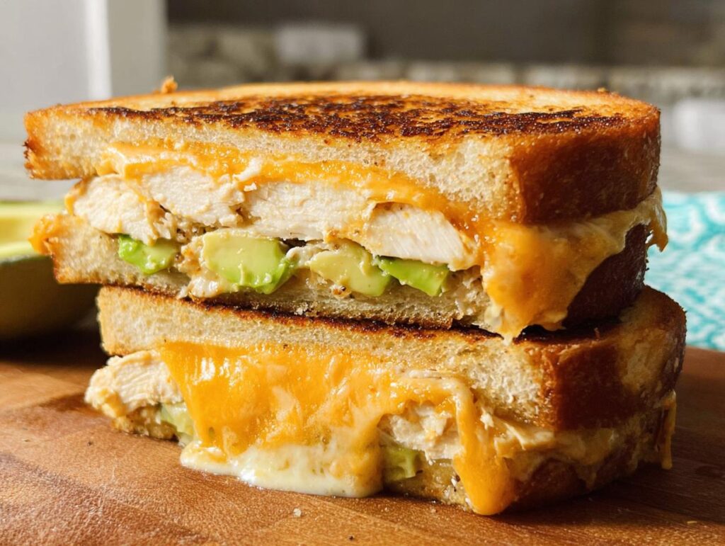 A close-up of a stacked Chicken Avocado Melt Sandwich, showing melted cheese, chicken, and avocado.