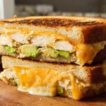 A close-up of a stacked Chicken Avocado Melt Sandwich, showing melted cheese, chicken, and avocado.