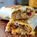 A cross-section of a Chicken Crunch Wrap showing seasoned chicken, rice, melted cheese, and red peppers.
