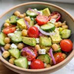 A vibrant bowl of Chickpea Feta Avocado Salad with cherry tomatoes, cucumber, red onion, and feta cheese.