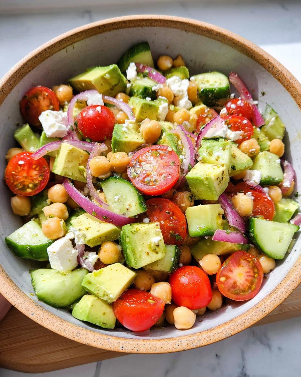 A vibrant bowl of Chickpea Feta Avocado Salad featuring diced avocado, cherry tomatoes, cucumber, red onion, feta cheese, and chickpeas.