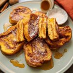 A plate of golden-brown Cinnamon Roll French Toast Bites drizzled with syrup and dusted with powdered sugar.