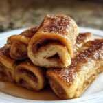 A stack of golden-brown Cinnamon Roll French Toast Roll-Ups dusted with powdered sugar and cinnamon.