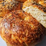 Close-up of golden brown cottage cheese flagels topped with sesame and black seeds, one sliced to show the fluffy interior.