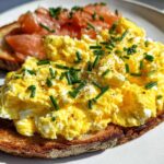 Close-up of Creamy Ricotta Egg Toast topped with scrambled eggs, chives, and smoked salmon.