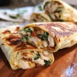 A close-up of a crispy chicken bacon wrap cut in half, revealing tender chicken, bacon, and spinach filling.