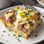 A slice of Easy Eggs Benedict Casserole topped with a fried egg, diced ham, hollandaise sauce, and chives.