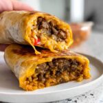 A close-up of an Easy Grilled Cheese Burrito Copycat Recipe, cut in half to show the cheesy beef and rice filling.