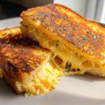 A perfectly grilled Garlic Bread Grilled Cheese sandwich, cut in half, with melted cheese oozing out.