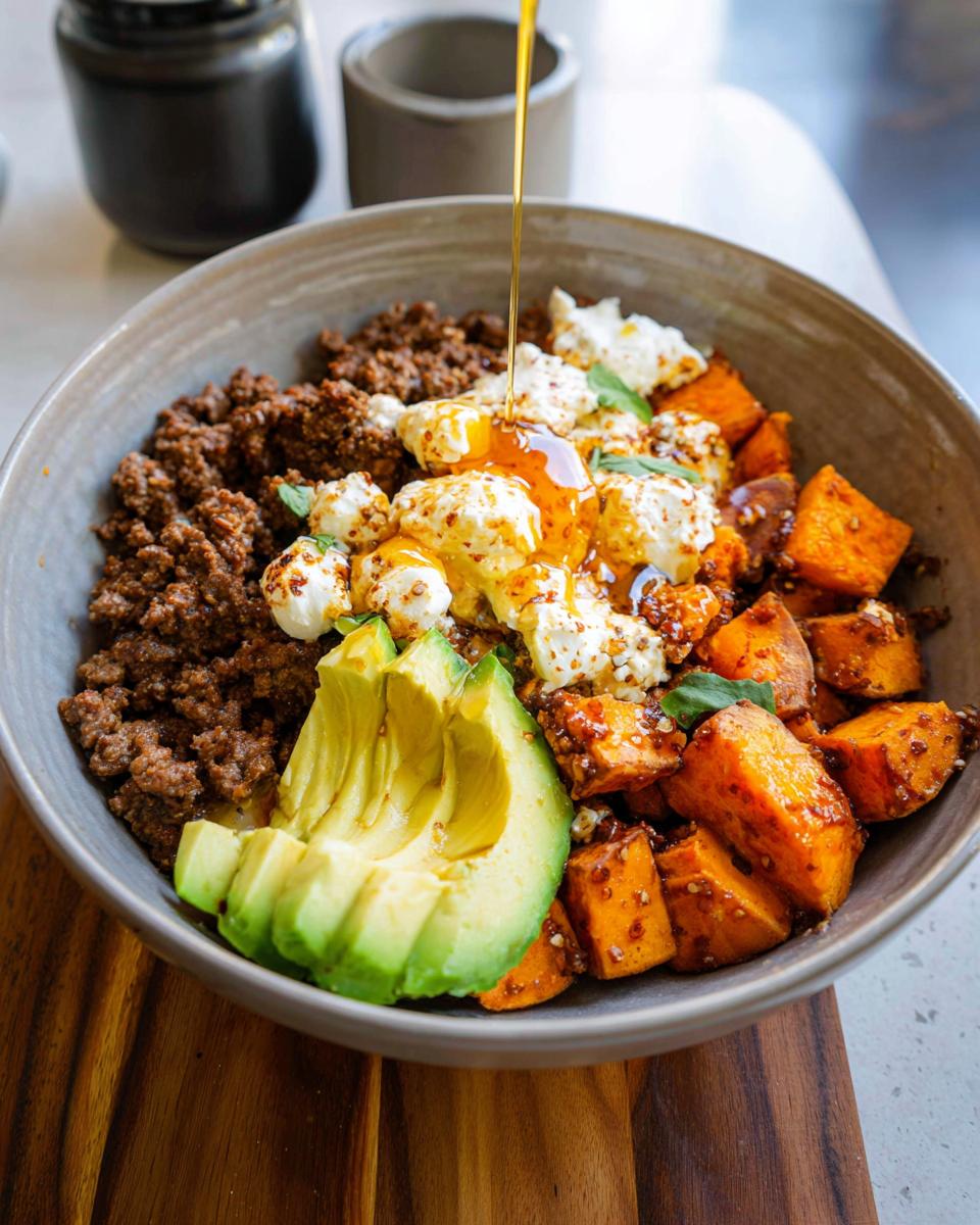 A delicious Ground Beef Hot Honey Bowl featuring seasoned ground beef, roasted sweet potatoes, avocado slices, and crumbled cheese with honey drizzled on top.