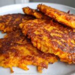 A close-up of golden brown, crispy Healthy Sweet Potato Hash Browns on a plate, with a dollop of sour cream and parsley.