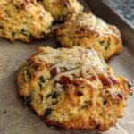 Close-up of golden-brown High Protein Breakfast Biscuits topped with melted cheese and visible herbs.
