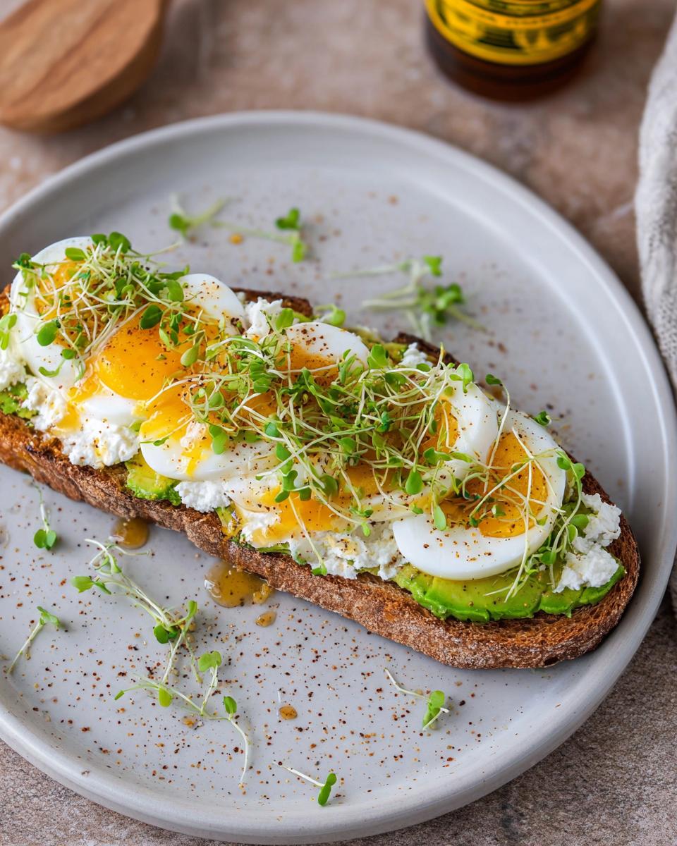 A high-protein breakfast toast topped with cottage cheese, avocado slices, hard-boiled eggs, and sprouts.
