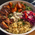 A delicious Hot Honey Chicken Bowl featuring sliced chicken, roasted sweet potatoes, quinoa, and a vibrant slaw with dressing.