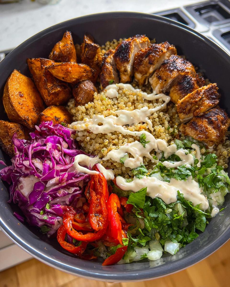 A vibrant Hot Honey Chicken Bowl Recipe featuring grilled chicken, quinoa, roasted sweet potatoes, red cabbage, and red peppers with a drizzle of sauce.
