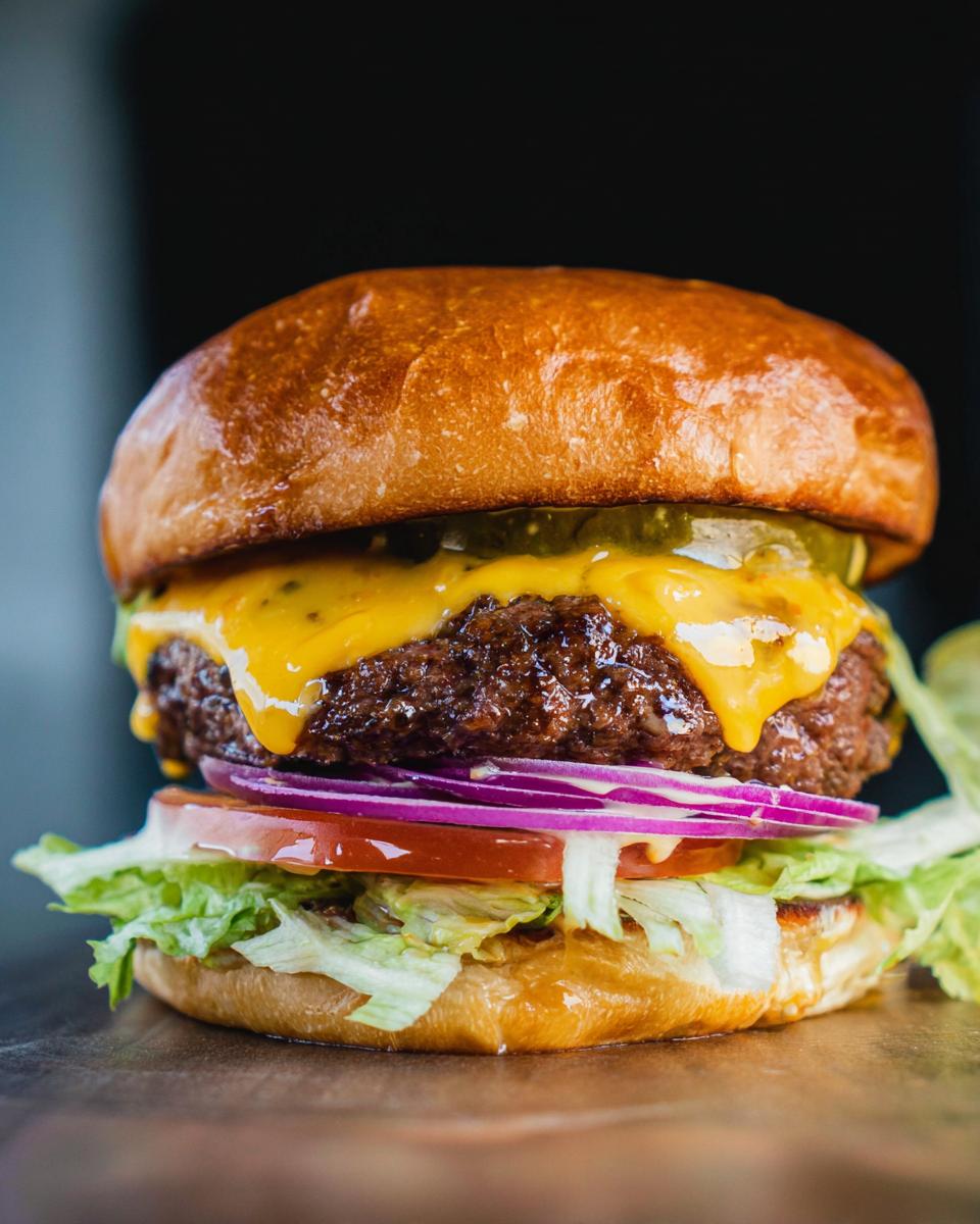 A close-up of an irresistible smash burger with melted cheese, pickles, lettuce, tomato, and red onion.
