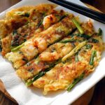 A close-up view of golden-brown Korean Pancakes (Pajeon) topped with succulent shrimp and green onions.