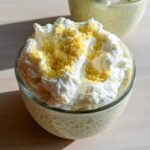 A close-up of a glass bowl filled with Lemon Cream Chia Pudding, topped with whipped cream and lemon zest.