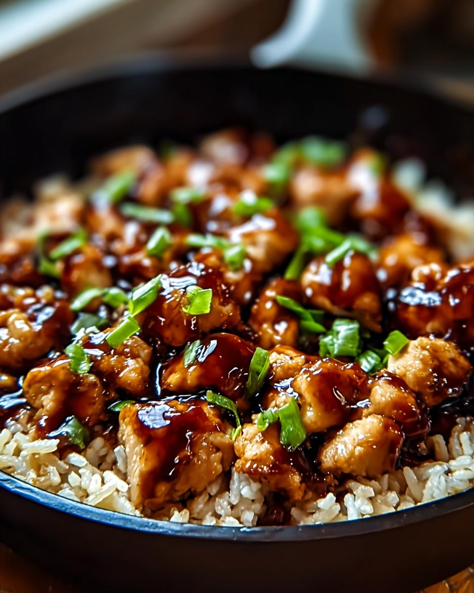 Close-up of a one-pan honey BBQ chicken rice dish, featuring tender chicken pieces coated in glossy BBQ sauce served over fluffy white rice, garnished with chopped green onions.