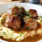 Close-up of Salisbury Steak Meatballs smothered in gravy, served over creamy Garlic Herb Mashed Potatoes and garnished with parsley.