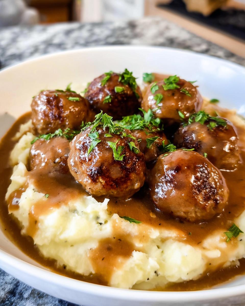 A close-up of Salisbury Steak Meatballs served over creamy Garlic Herb Mashed Potatoes, garnished with parsley.