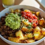 A close-up of a Schnelle Kartoffel Taco Bowl Meal Prep featuring seasoned potatoes, ground meat, guacamole, and salsa.