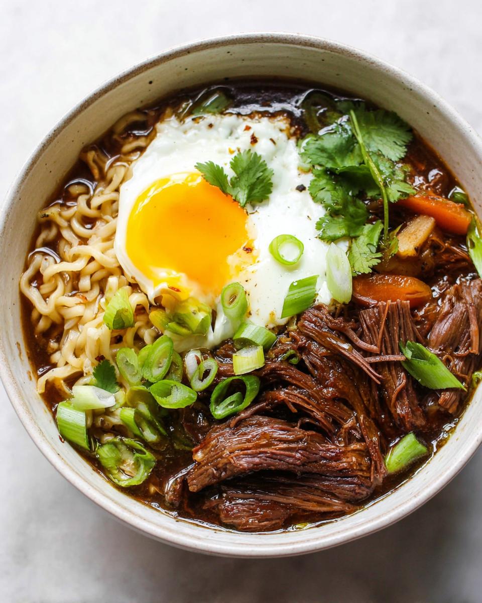 A delicious bowl of Slow Cooker Beef Ramen Noodles topped with a fried egg, shredded beef, and green onions.