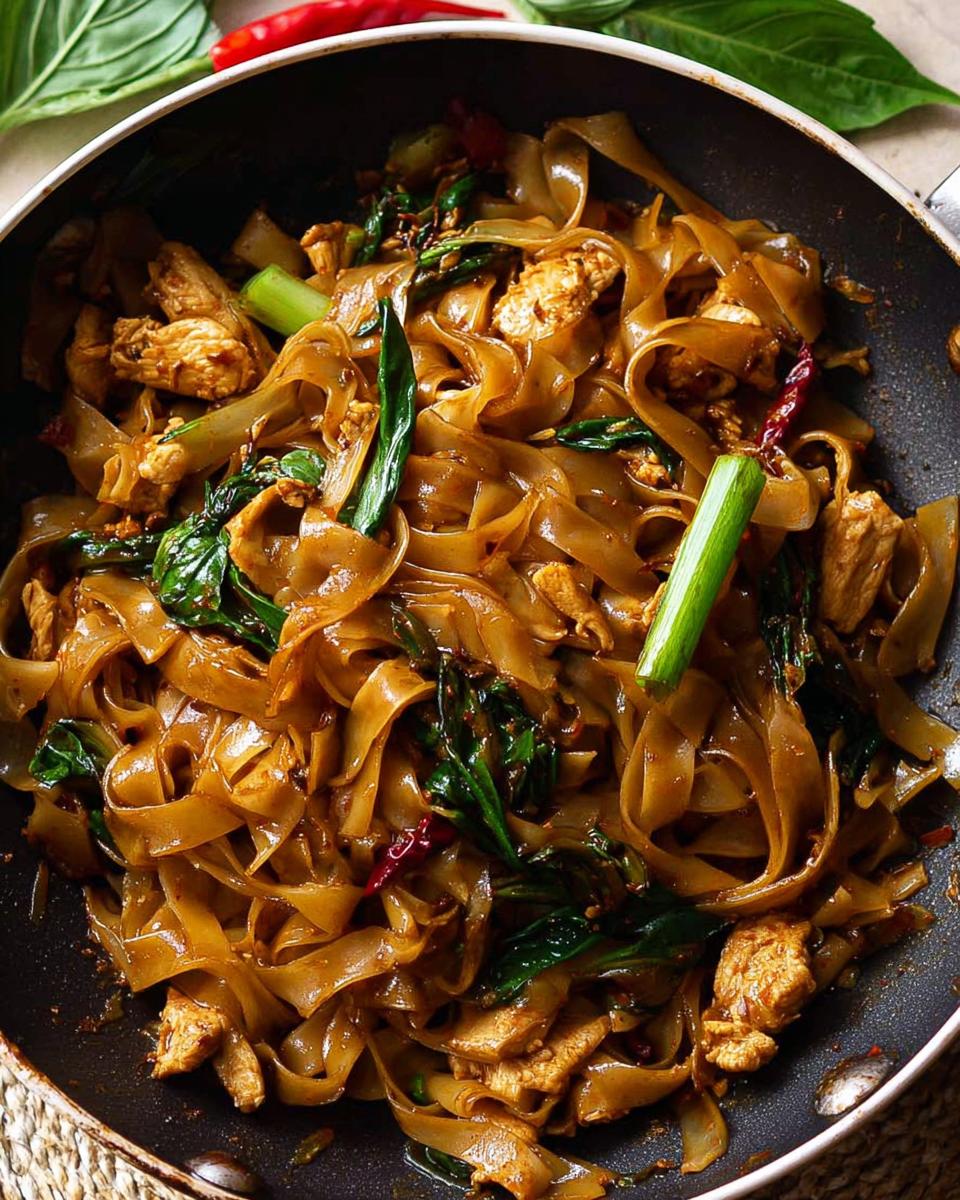 Close-up of Street Style Thai Drunken Noodles with chicken, wide rice noodles, and basil in a pan.
