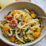 A bowl of delicious Tomato Zucchini Pasta, featuring fresh cherry tomatoes, sliced zucchini, and pasta in a creamy sauce, topped with grated cheese and black pepper.