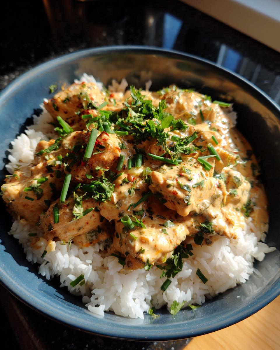 A close-up view of a Creamy Cajun Chicken & Rice Bowl, featuring tender chicken in a rich sauce served over fluffy white rice, garnished with fresh herbs.