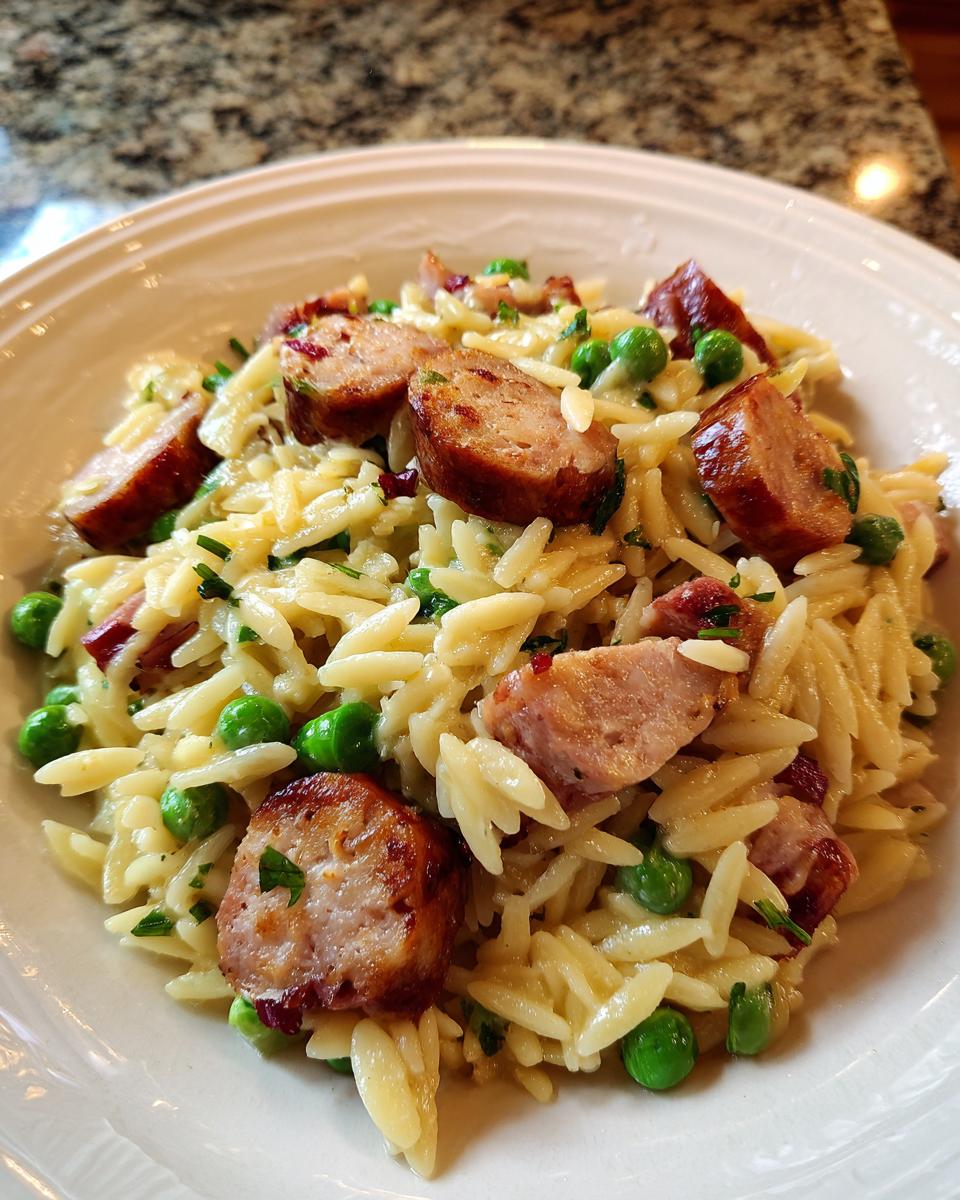 A close-up of a bowl of Creamy Chicken Sausage Orzo, featuring pasta, sliced sausage, and peas.