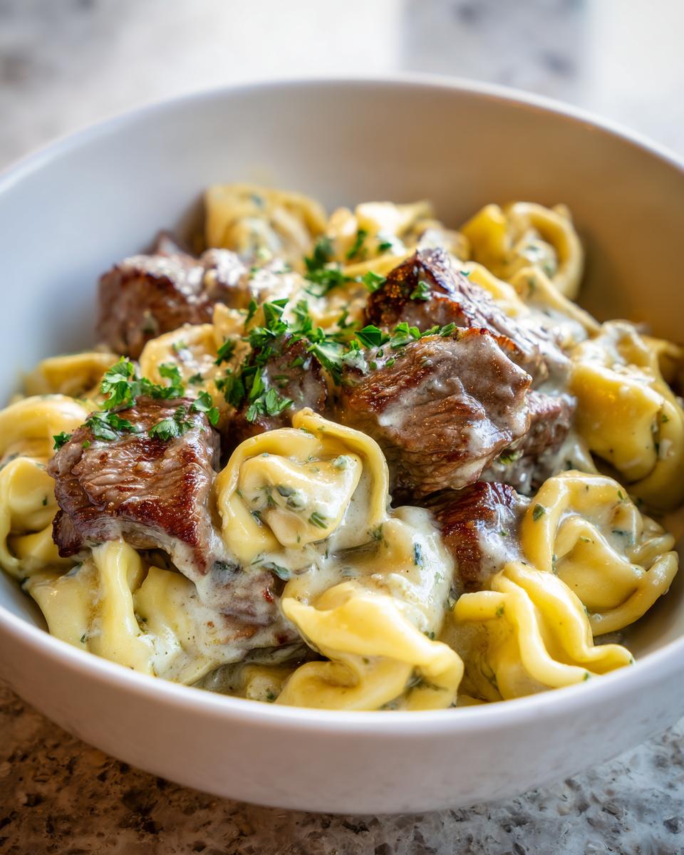 A close-up of a bowl of Garlic Steak Tortellini, featuring tender steak pieces and tortellini pasta in a rich, creamy sauce, garnished with parsley.