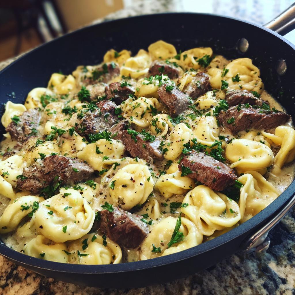 A close-up of Garlic Steak Tortellini in a creamy sauce, garnished with fresh parsley, served in a black skillet.