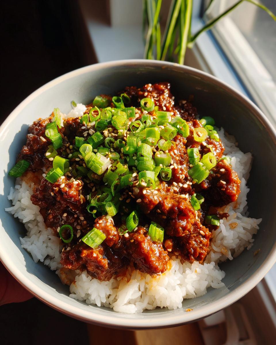 A close-up of a Korean Ground Beef Bowl, featuring fluffy white rice topped with savory ground beef and garnished with chopped green onions and sesame seeds.