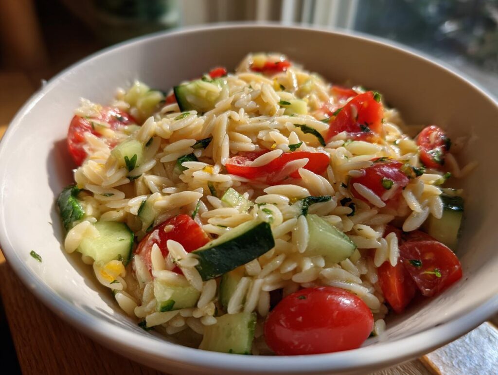 A bowl of lemony orzo salad with fresh cherry tomatoes and cucumber, perfect for summer salad recipes.