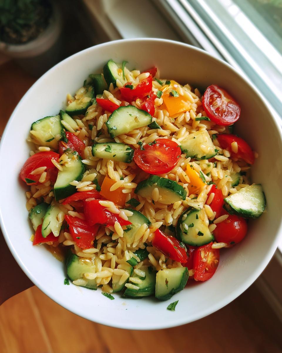 A bowl of lemony orzo salad with fresh chopped cucumber, cherry tomatoes, and bell peppers.