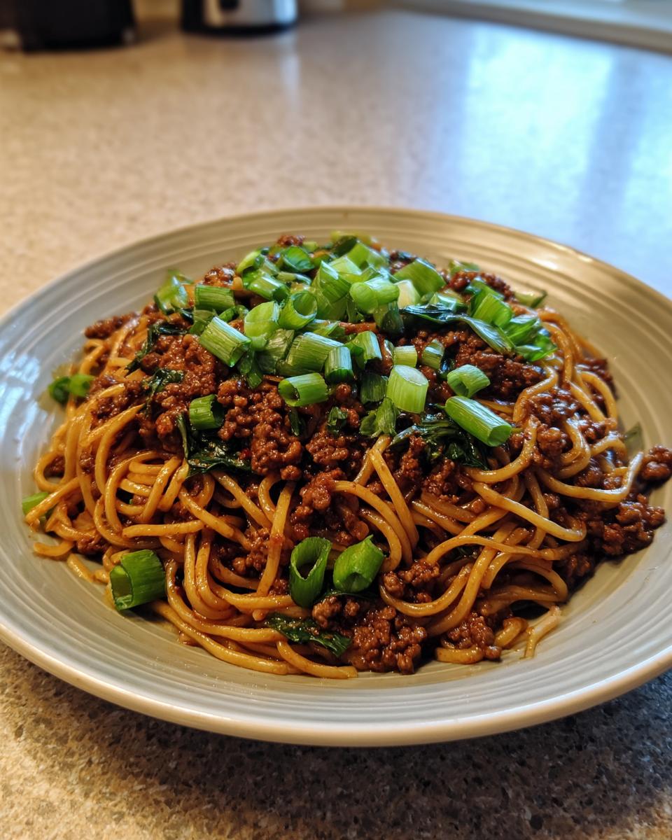 A close-up of a bowl of Mongolian Ground Beef Noodles, topped with fresh green onions.