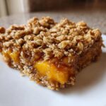 A slice of peach crumble bars with a buttery oat topping, showcasing the juicy peach filling.